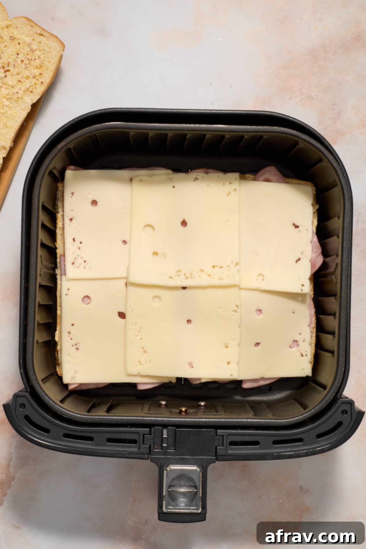Swiss cheese placed on top of ham in the air fryer basket.