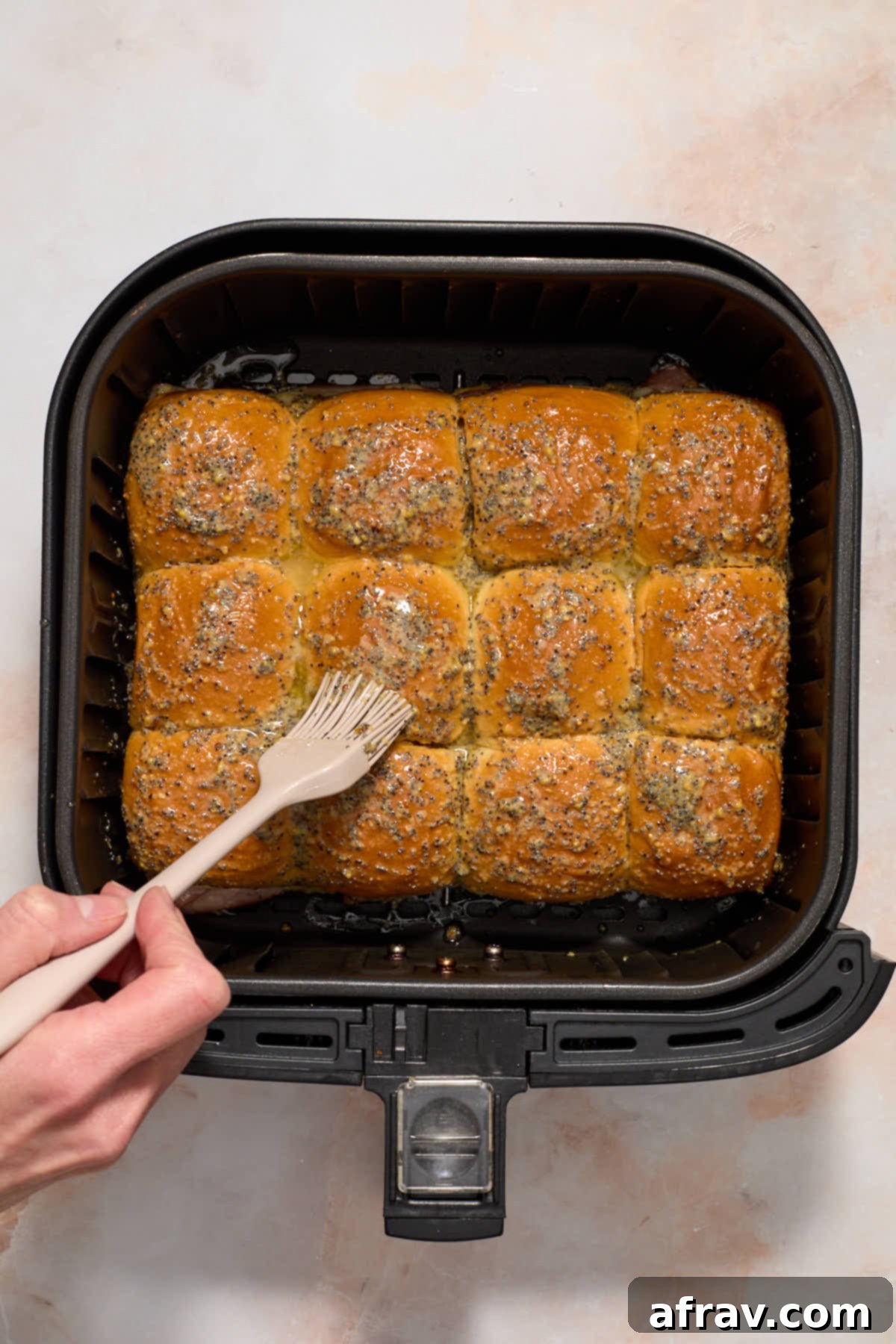 Brushing butter mixture on top of assembled sliders inside the air fryer basket.