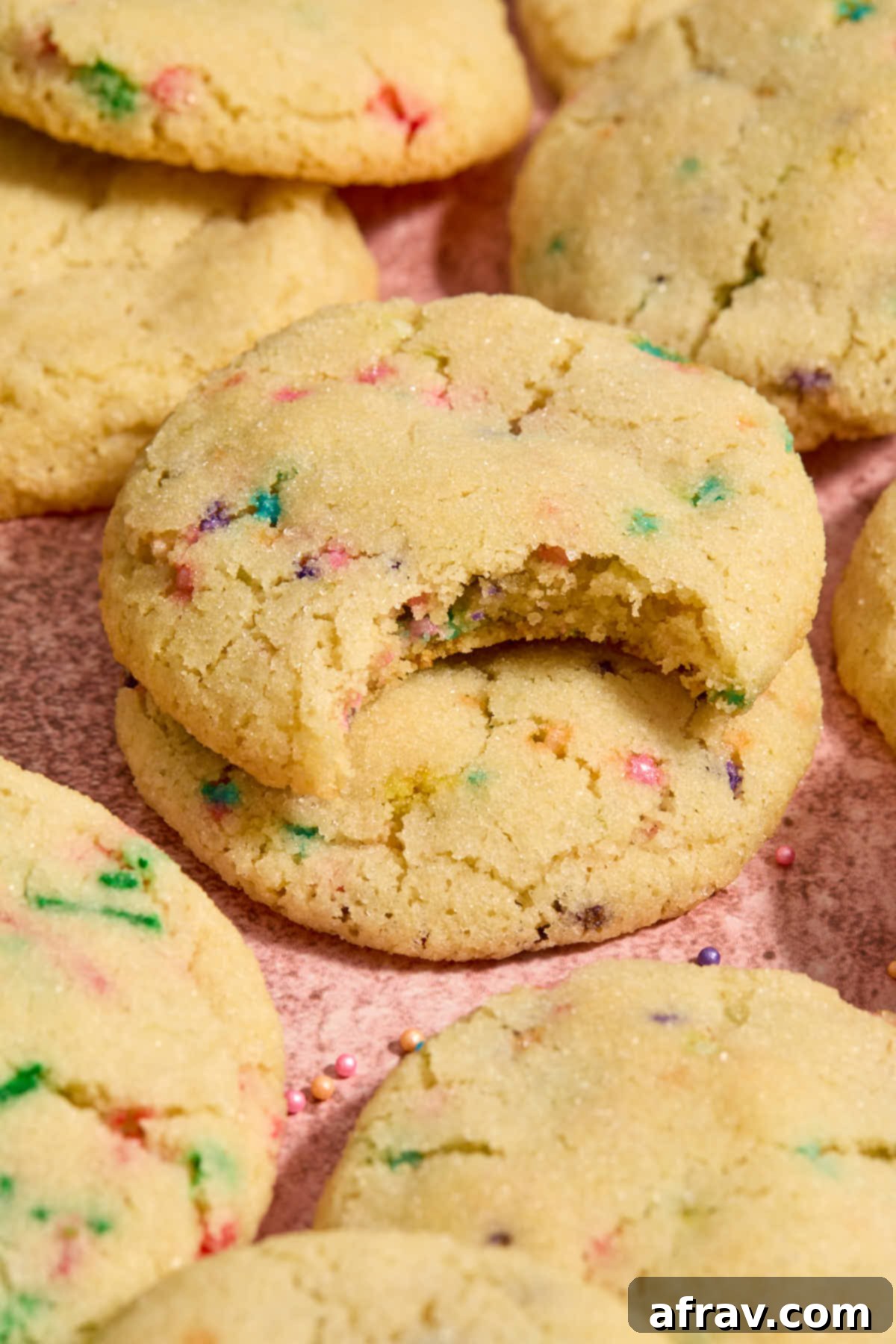 A plate of almond flour sugar cookies, some with sprinkles, arranged on a pink surface with one cookie having a bite taken out.
