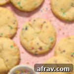 Almond flour sugar cookies (with sprinkles) arranged on a pink surface with a bowl of sprinkles on the side. These gluten-free treats are soft, chewy, and easy to make.