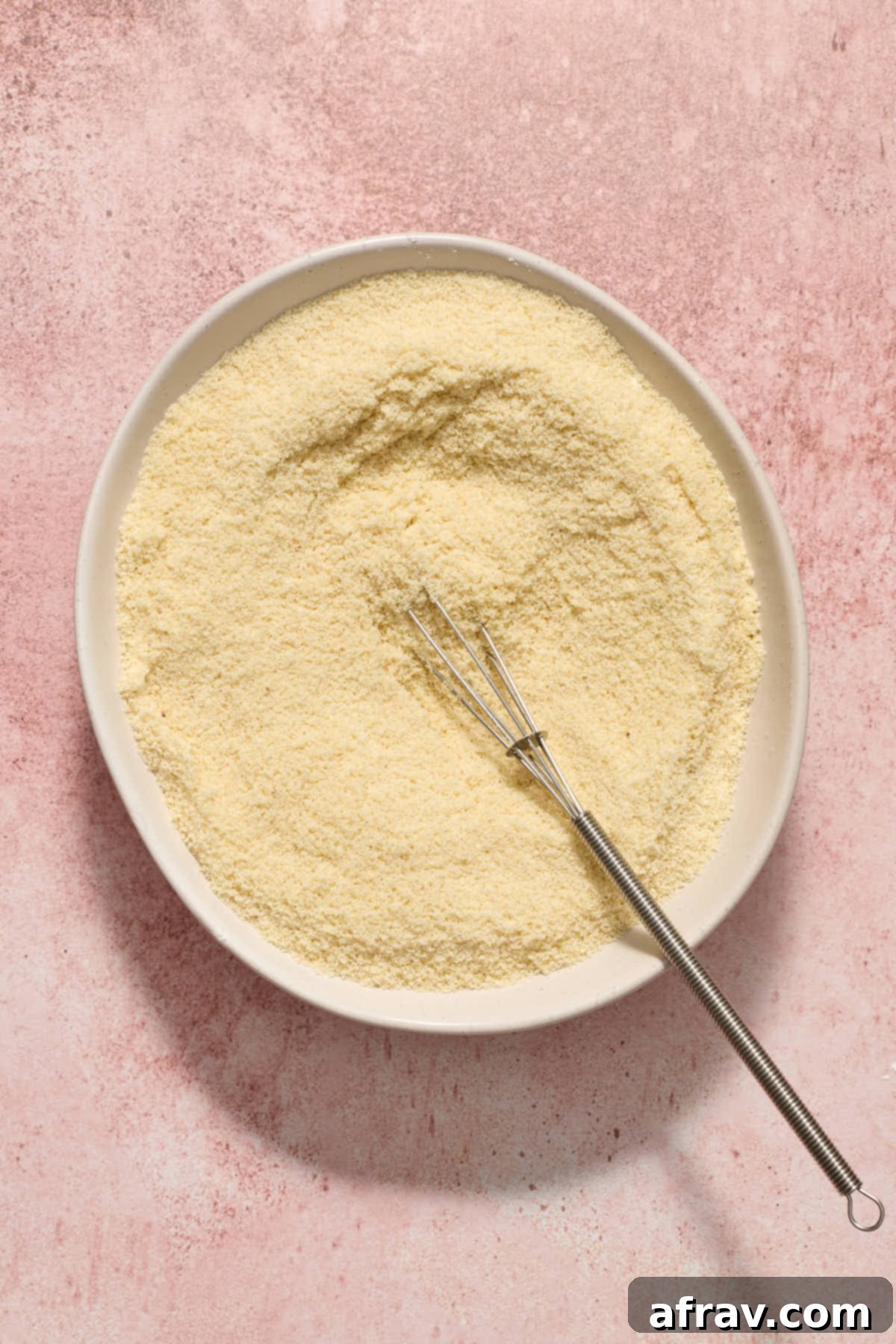 Dry ingredients including almond flour, cornstarch, baking soda, and salt whisked together with a small whisk in a white bowl.