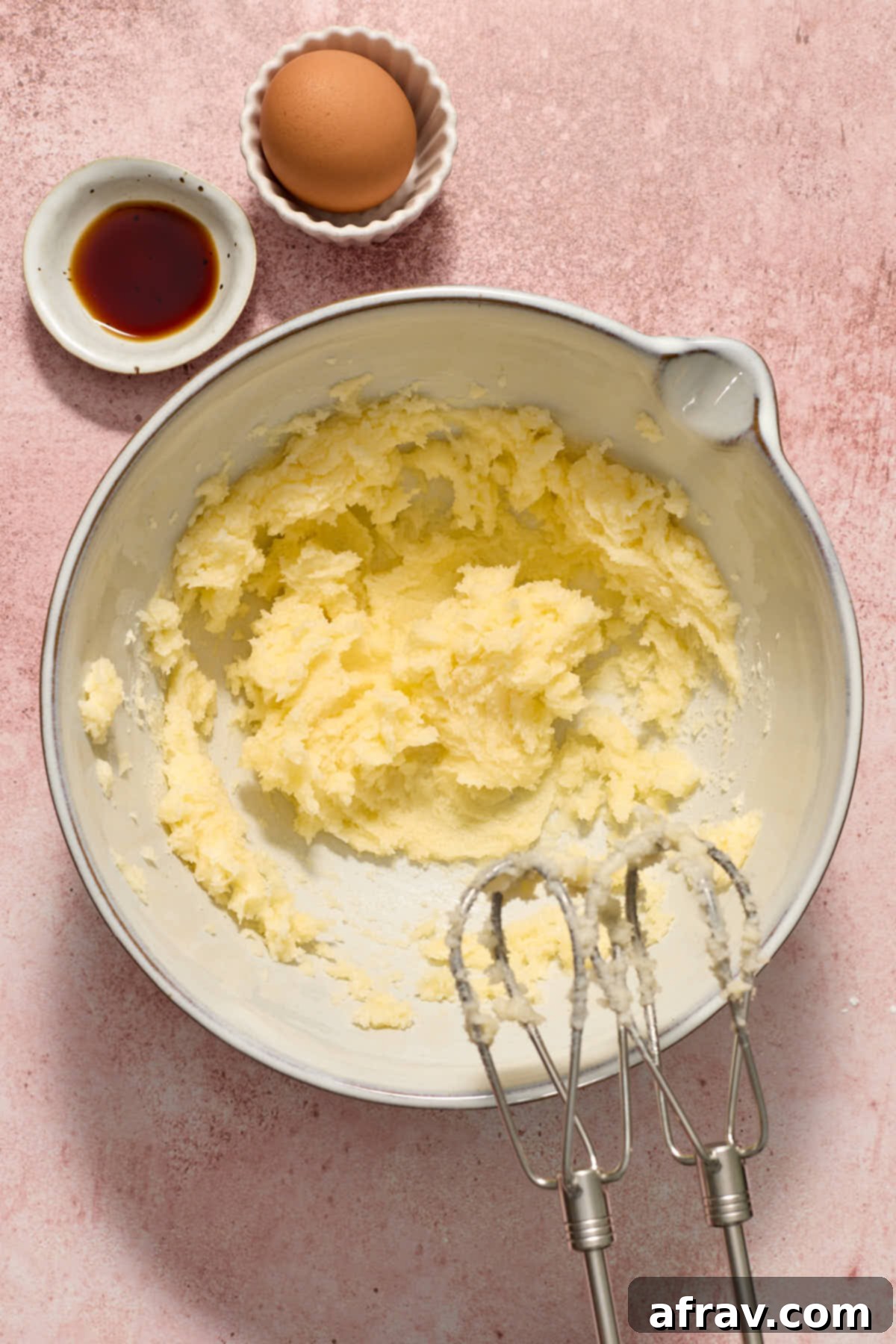 Granulated sugar and softened unsalted butter creamed together in a mixing bowl with egg and vanilla extract waiting nearby.