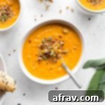 Overhead view of Roasted Red Pepper and Butternut Squash Soup in white bowls and mugs, garnished with fresh herbs.
