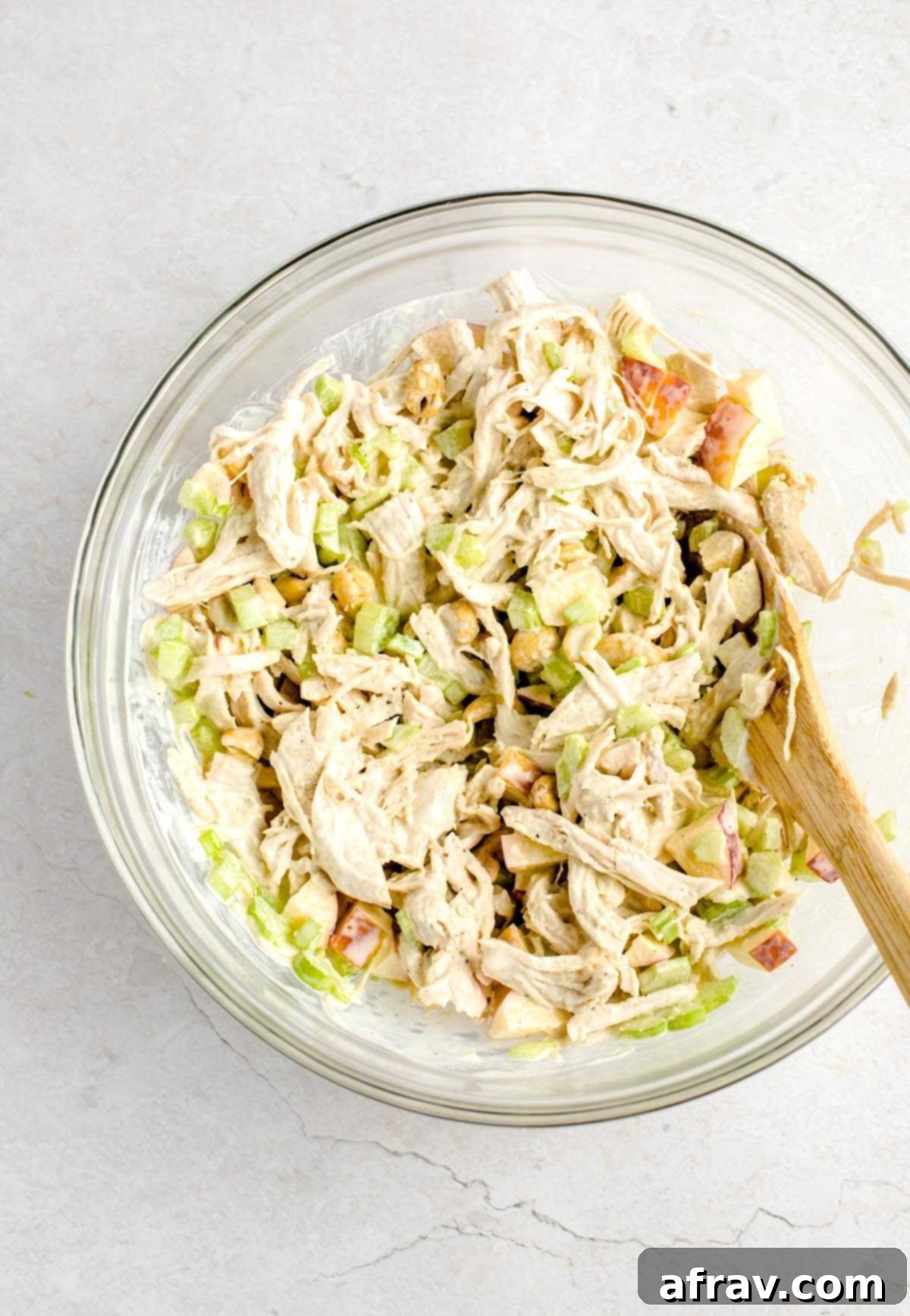 Chicken salad being mixed in a bowl, showing the creamy coating.