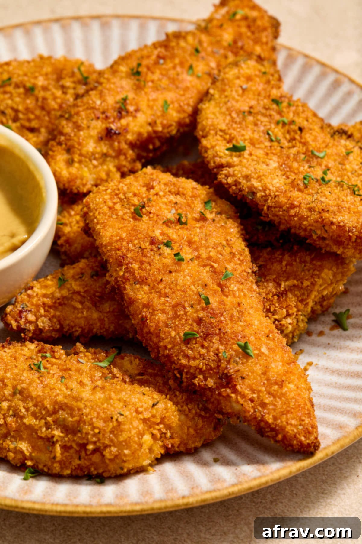 Angled view of air fried chicken strips on a plate with a small dish of honey mustard.