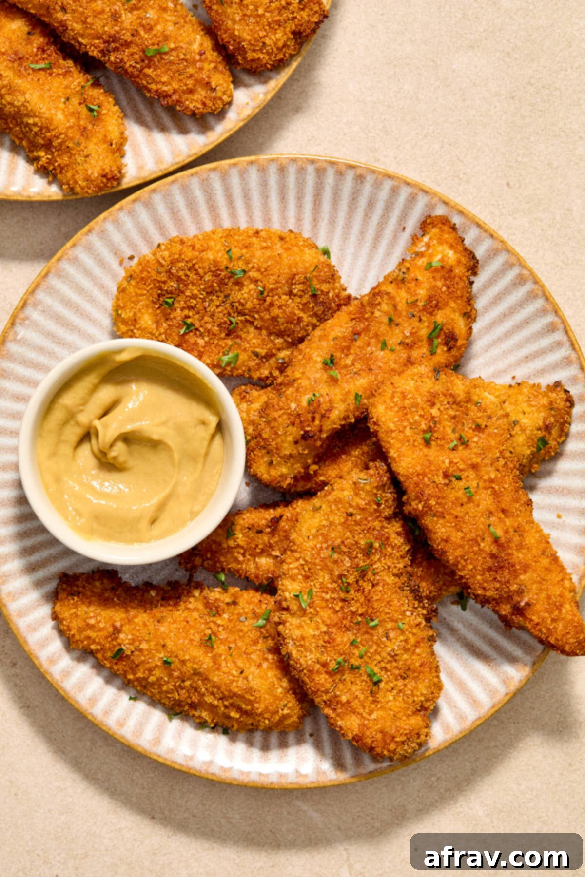 Chicken strips served on a plate with honey mustard on the side for dipping.