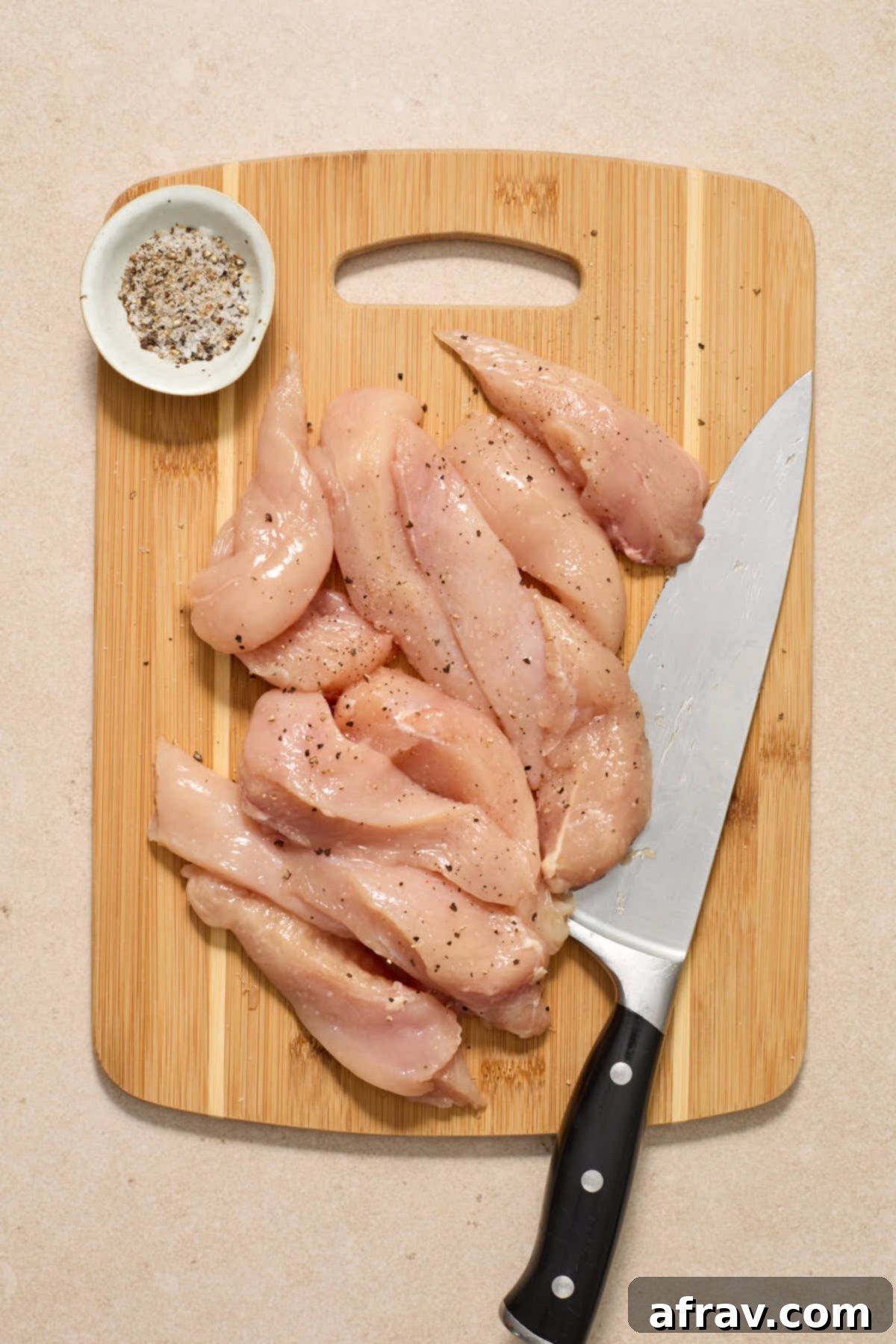 Chicken breasts cut into slices on a bamboo cutting board and seasoned with salt and pepper.