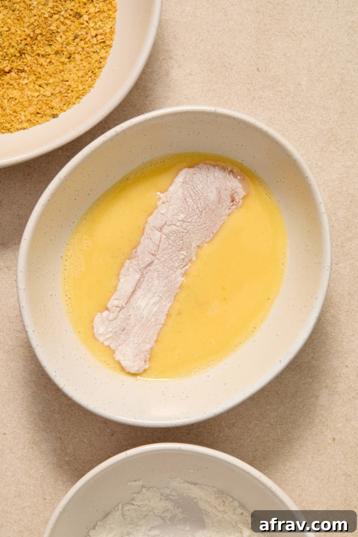 Floured chicken strip being dipped in the egg/milk mixture.