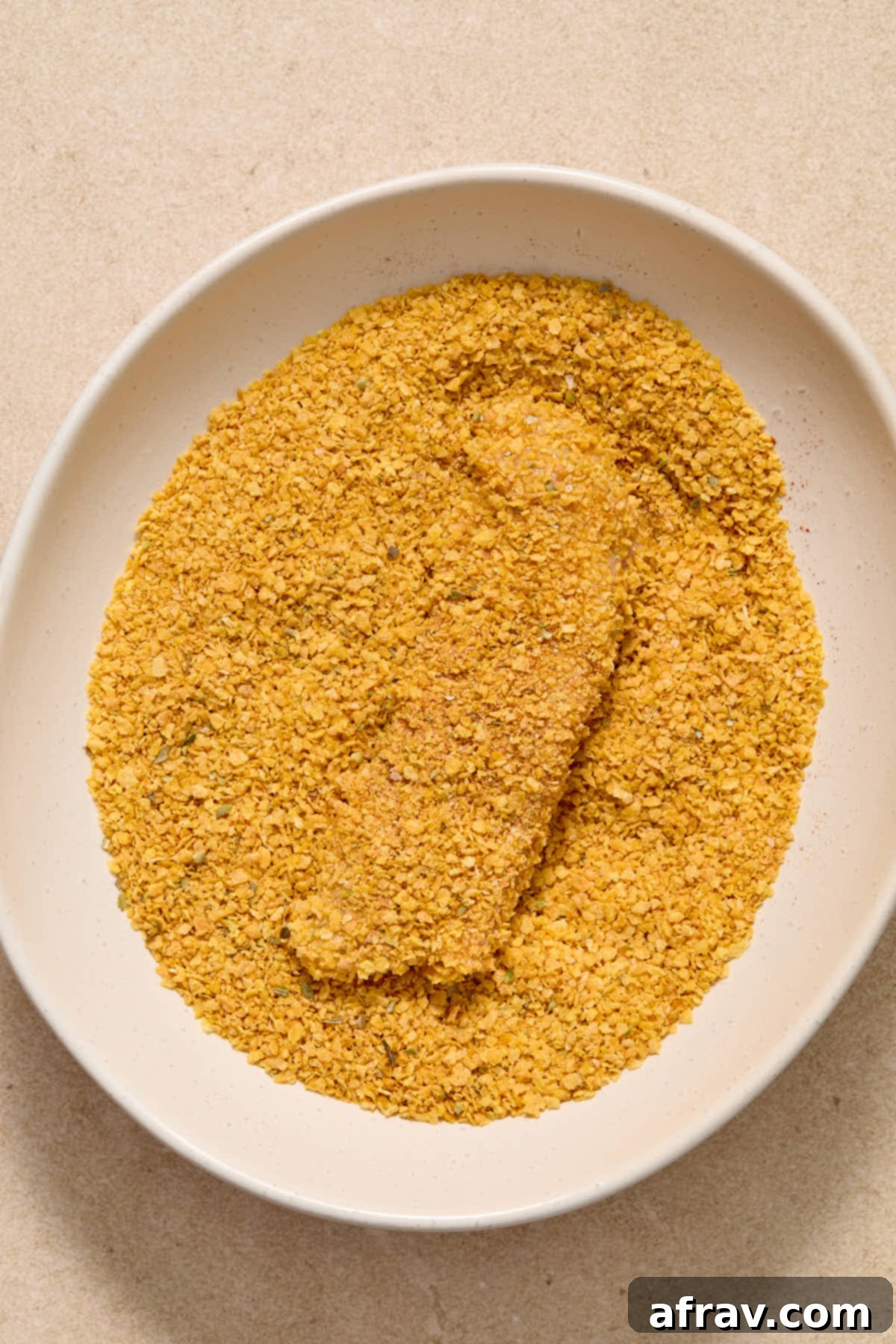 A chicken strip being coated in the cornflake crumb mixture.