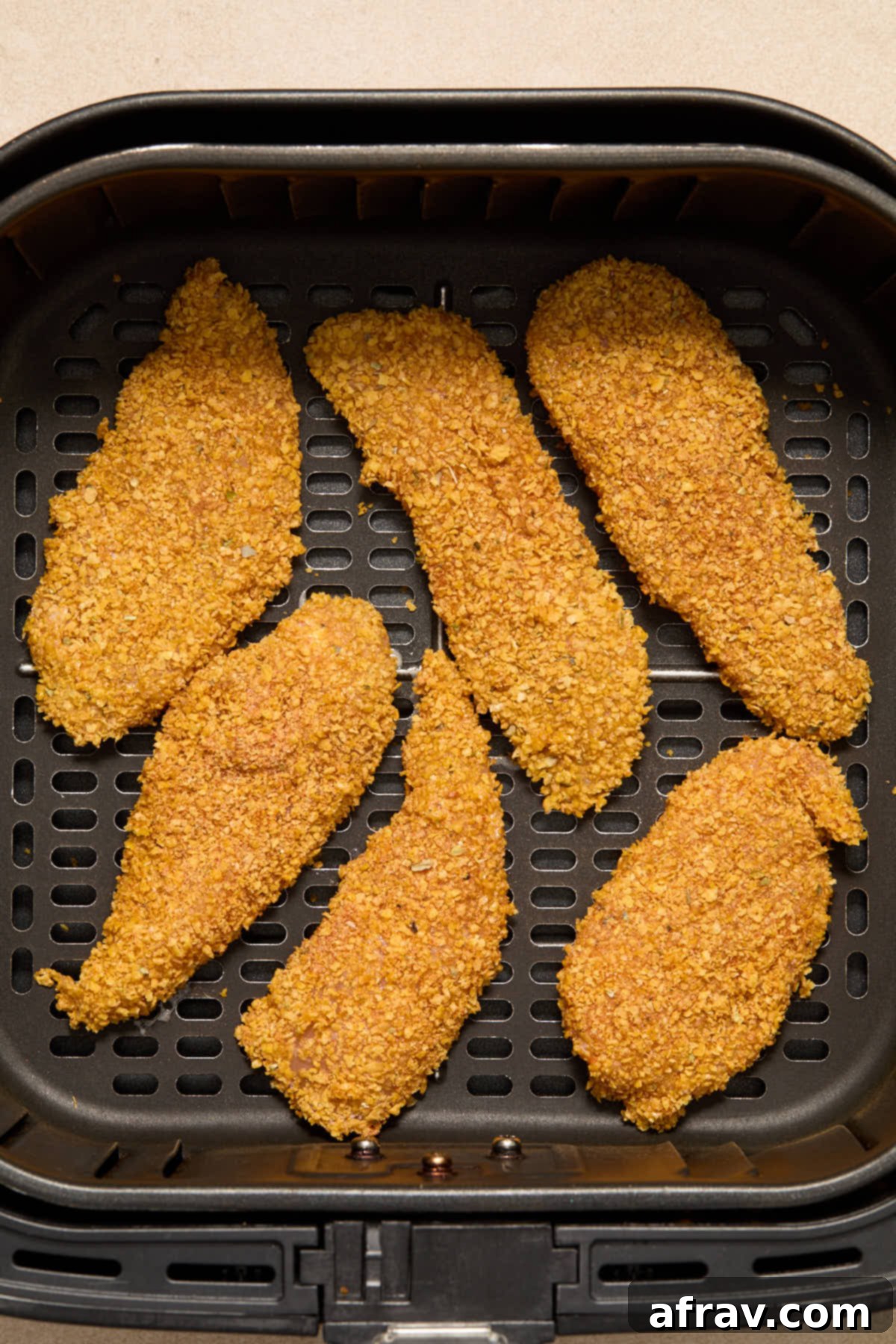 Cornflake crusted chicken strips arranged in a single layer in the air fryer basket.
