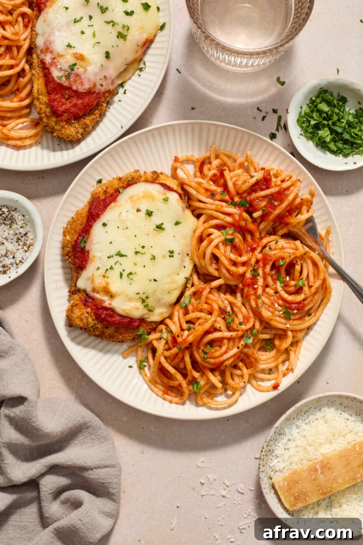 Parmesan chicken served on plates with spaghetti and marinara sauce.