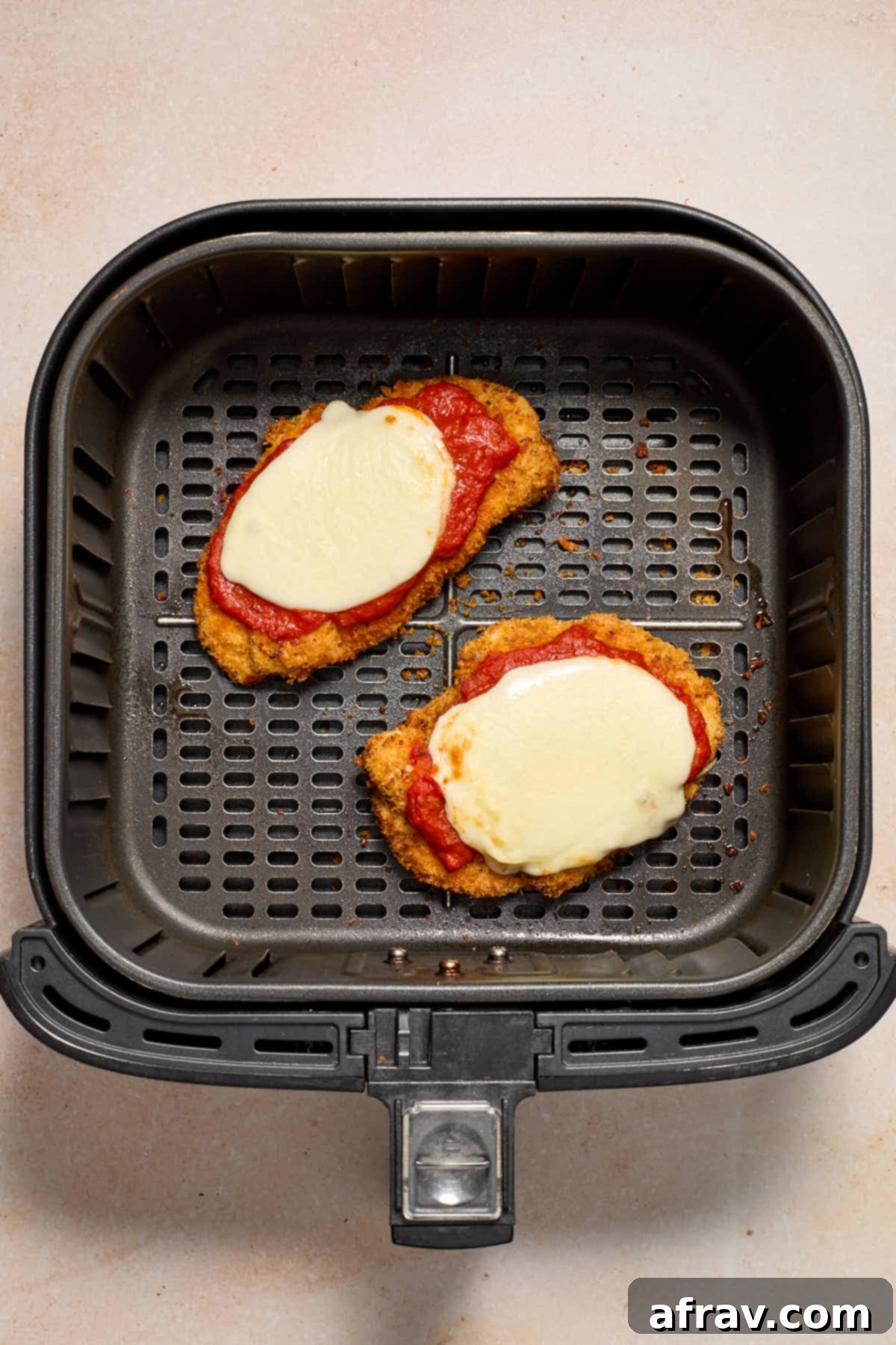Finished chicken in the air fryer basket with marinara and melted mozzarella cheese on top.