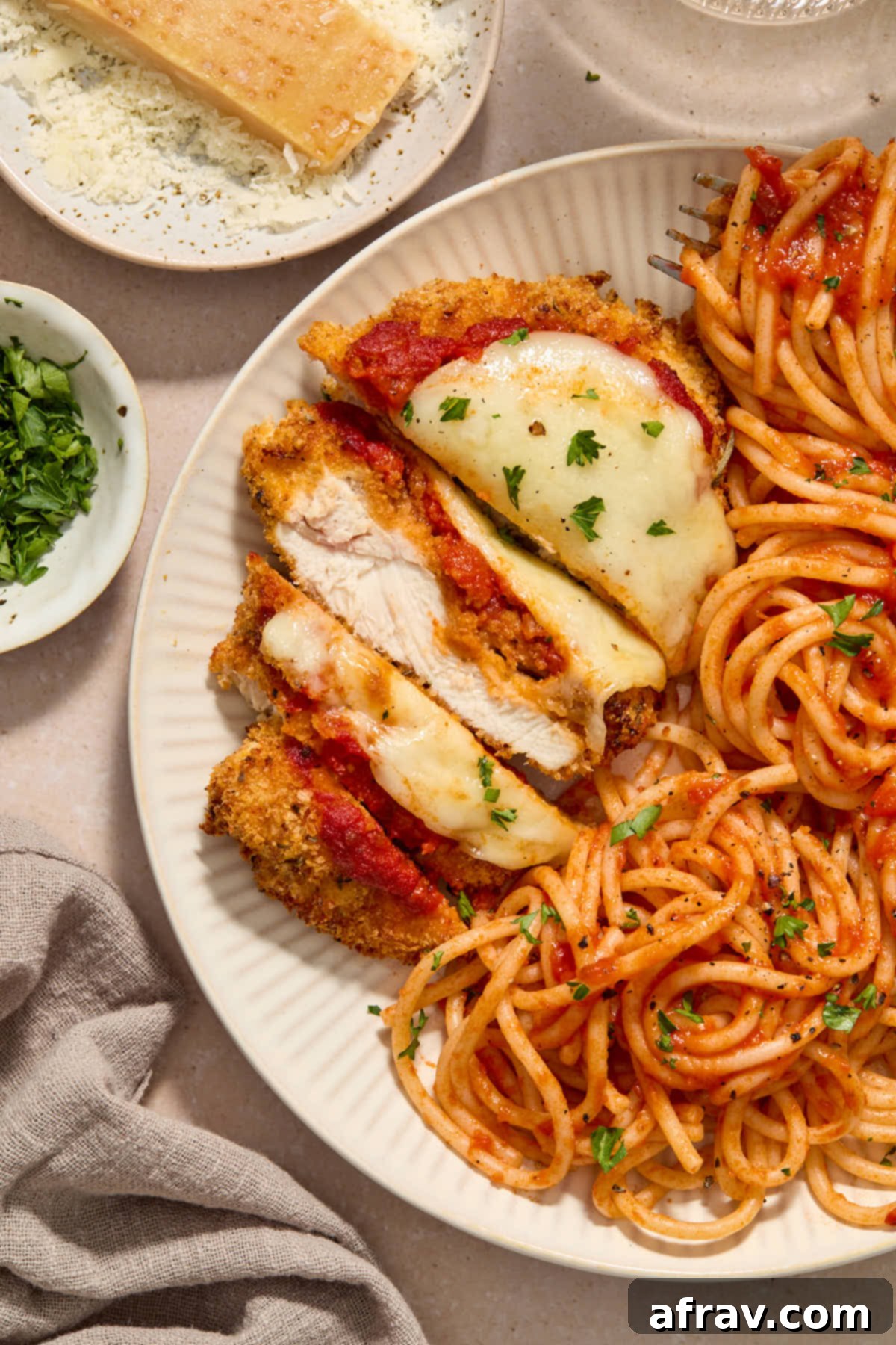 Close up of a piece of parmesan chicken sliced on a plate and served with spaghetti.