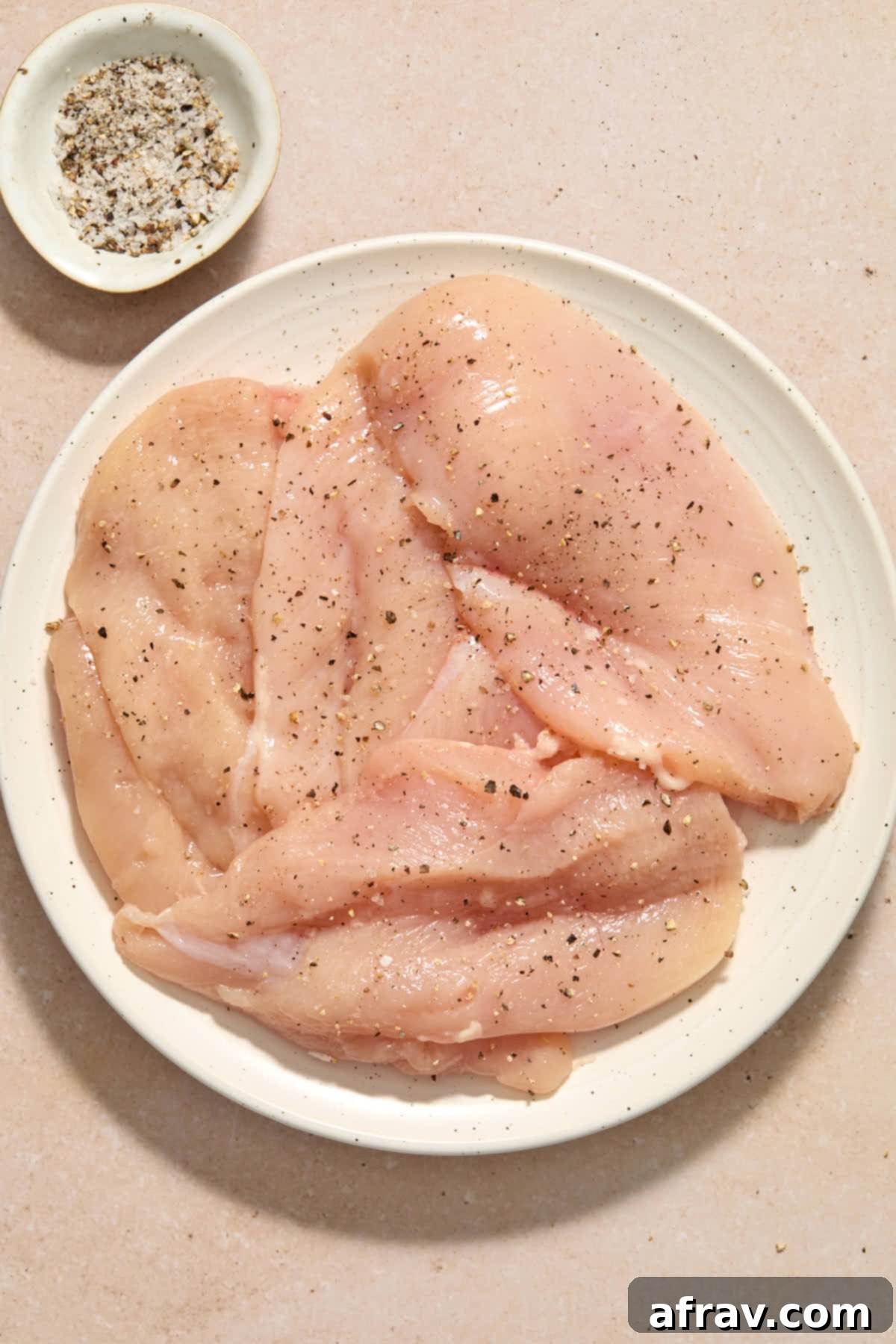 Chicken breasts cut in half lengthwise, placed on a plate and seasoned with salt and pepper.