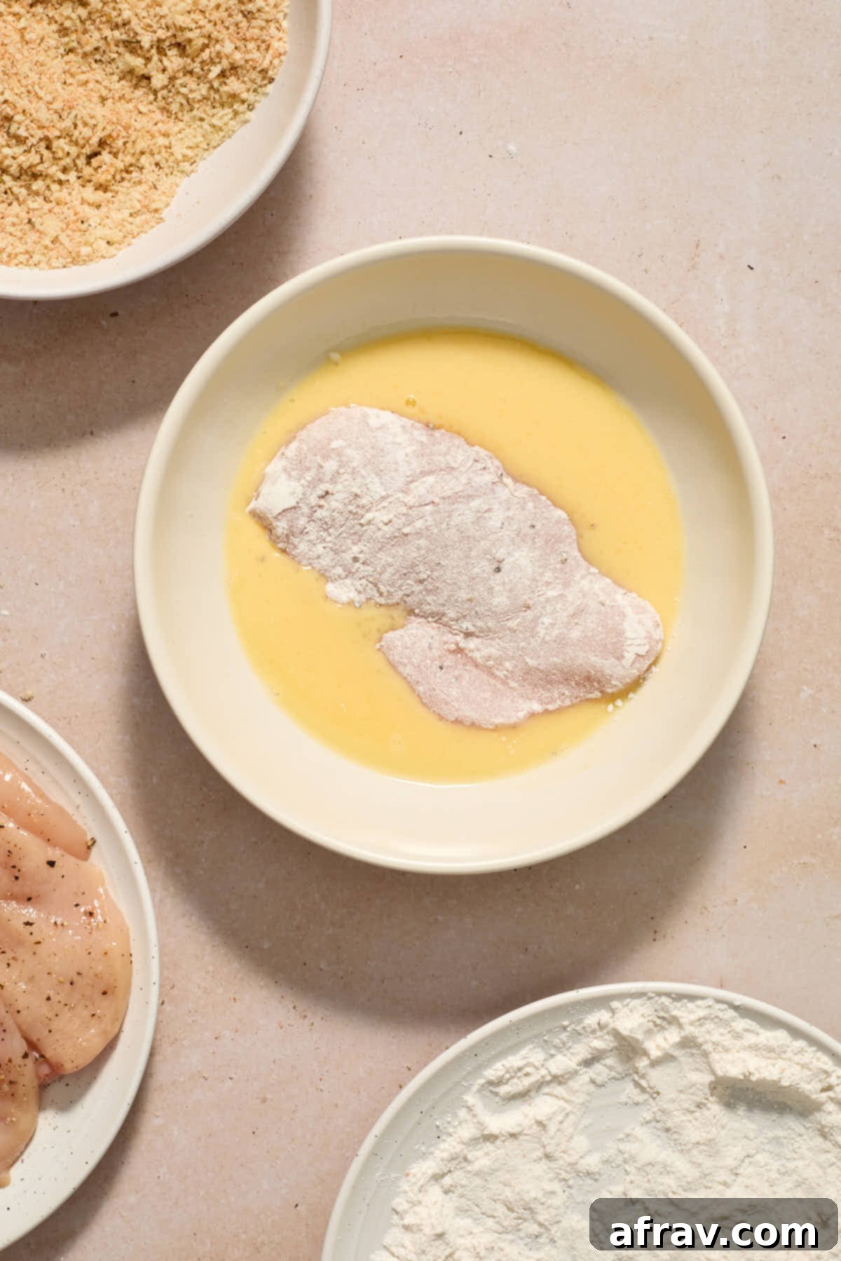Piece of floured chicken being coated in the egg mixture.