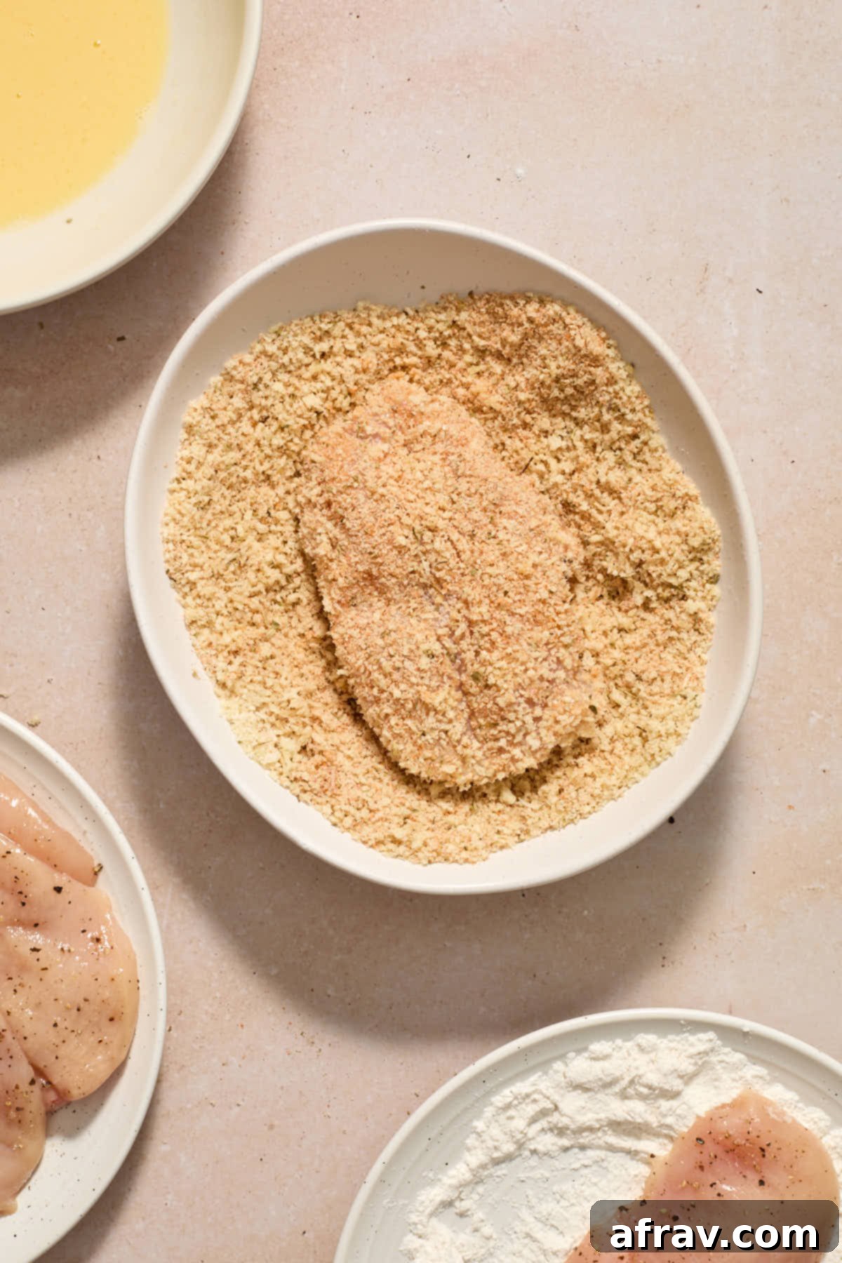 Piece of chicken coated in the panko crumb mixture in a shallow bowl.