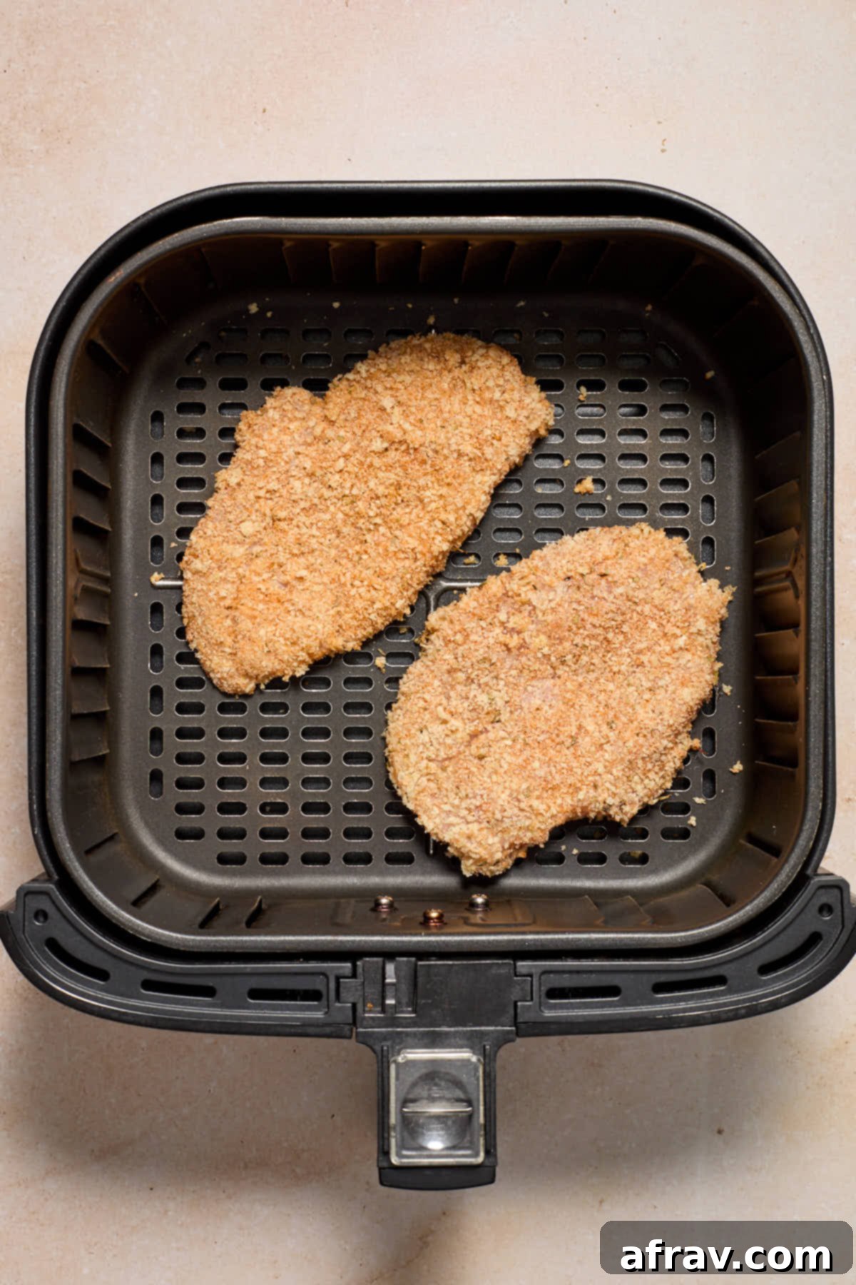 Two breaded pieces of chicken uncooked in the air fryer basket.