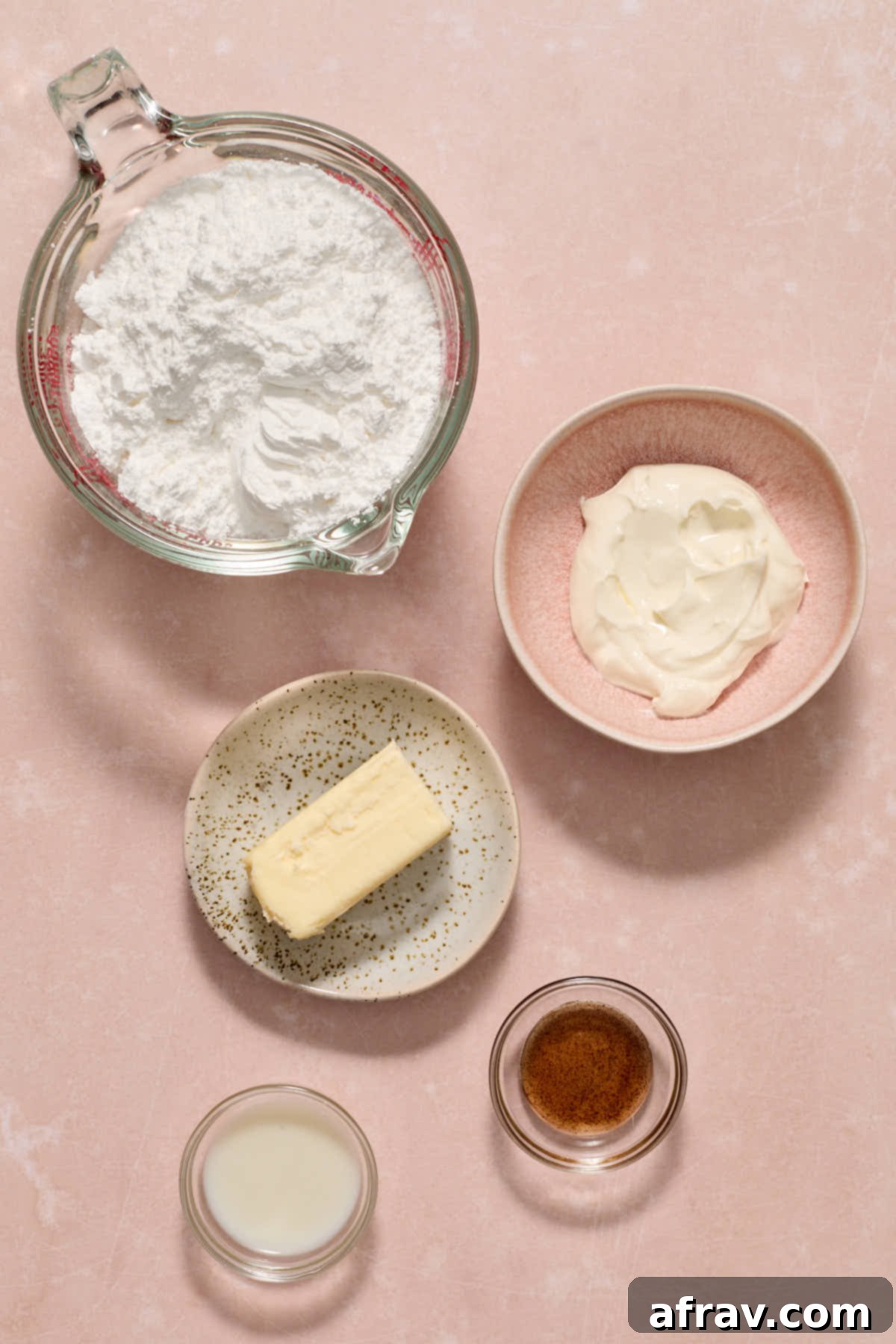 Double Sour Cream Banana Cake 4 Key ingredients for the sour cream frosting, like butter, powdered sugar, and sour cream, neatly arranged on a pink surface.