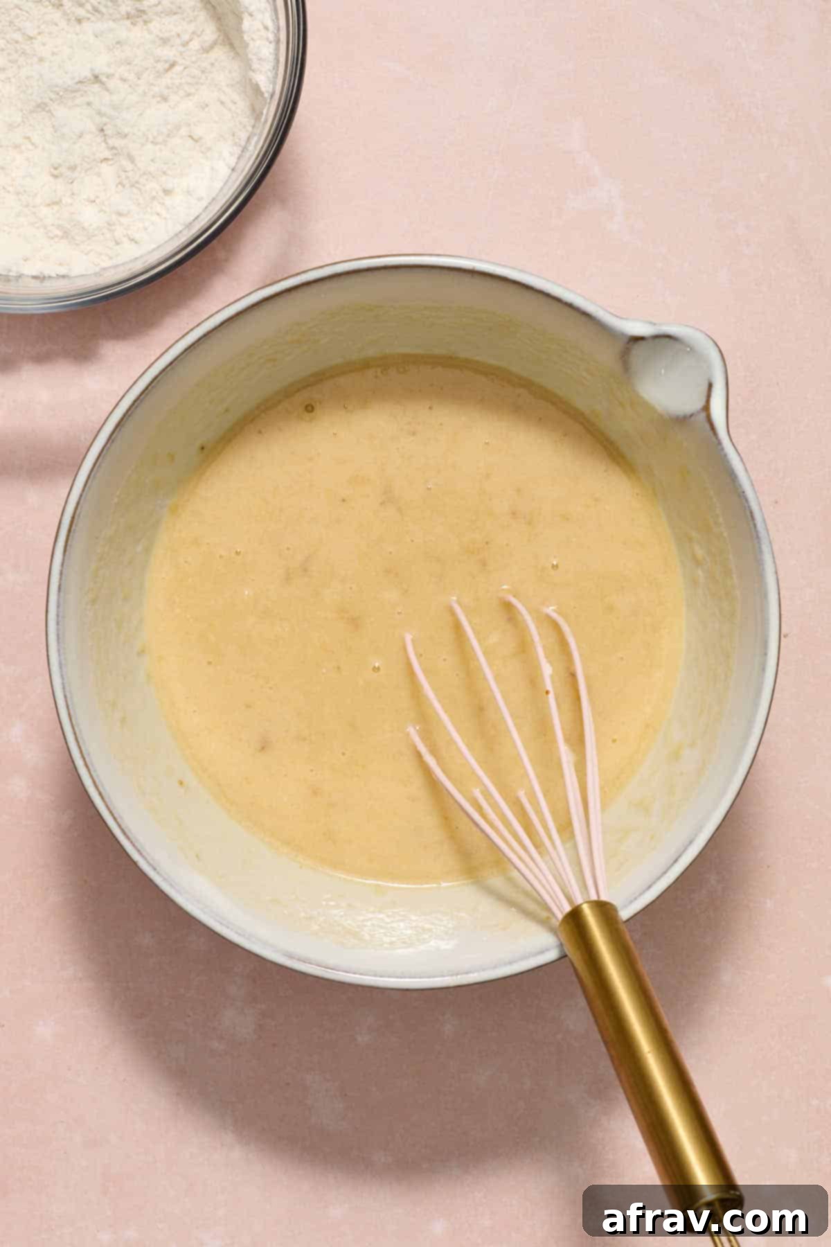 Double Sour Cream Banana Cake 7 All wet ingredients—mashed banana, sour cream, egg, and vanilla—are whisked into the sugar and oil mixture in a white bowl, forming a smooth, uniform liquid.