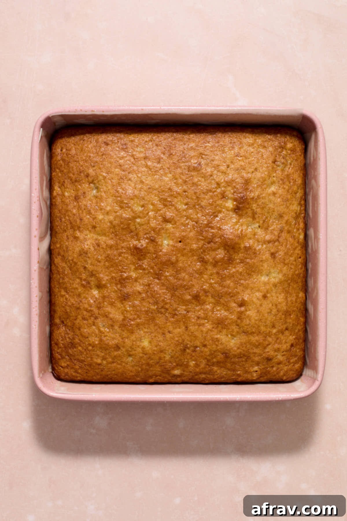 Double Sour Cream Banana Cake 10 A perfectly golden-brown banana cake, freshly baked in its square pan, with edges slightly pulled away, indicating it's done.
