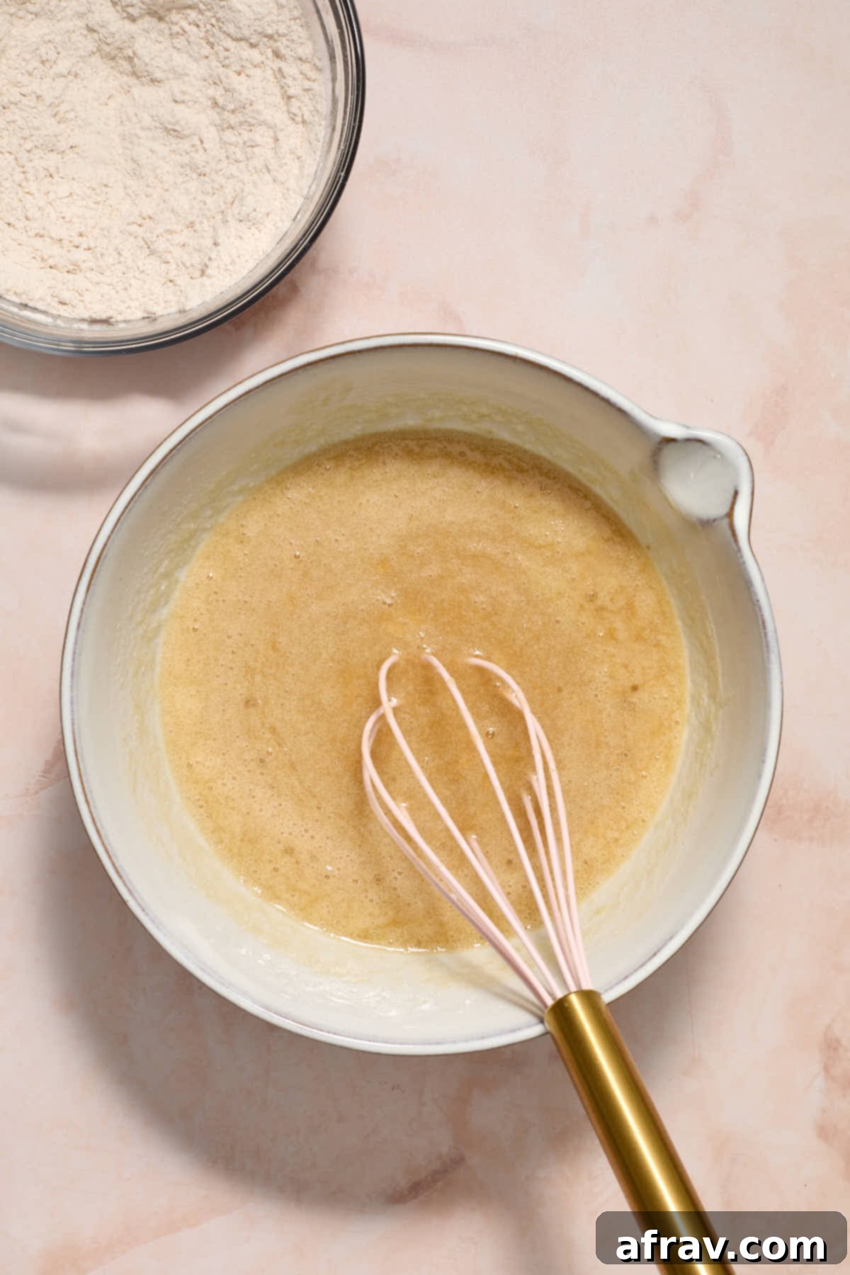 Wet ingredients whisked together in a white bowl with the dry ingredients to the side.