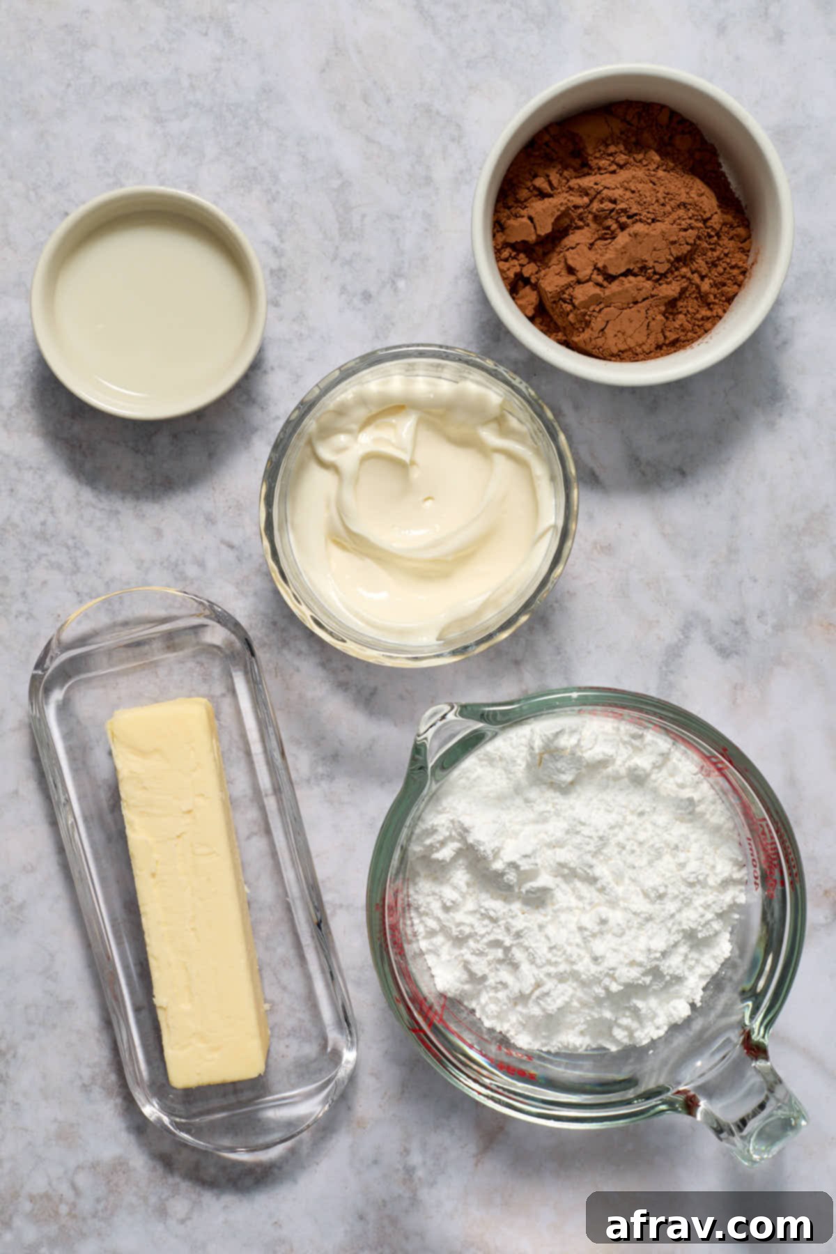 Individual ingredients for sour cream chocolate frosting, including butter, cocoa, powdered sugar, and sour cream, neatly arranged.