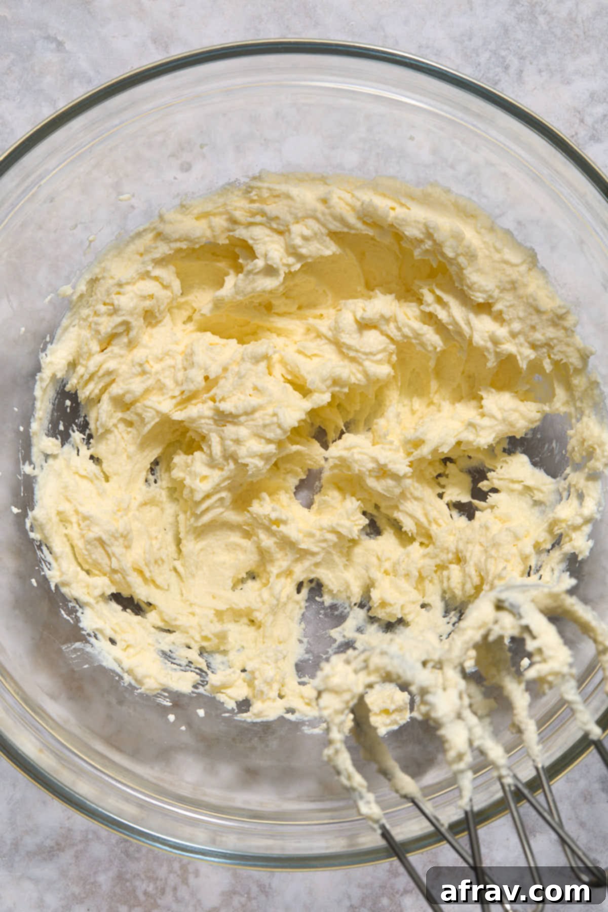 Room temperature sour cream and butter being creamed together in a clear glass mixing bowl with an electric mixer.