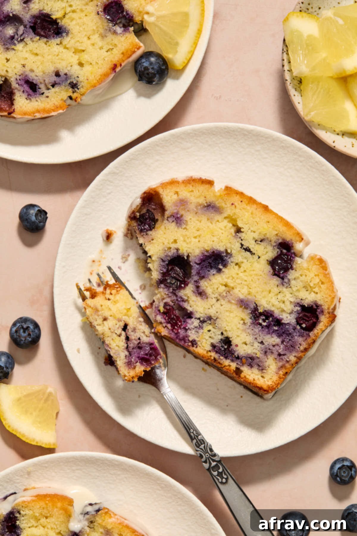 Slices of blueberry bread on white plates with lemon slices on the side.