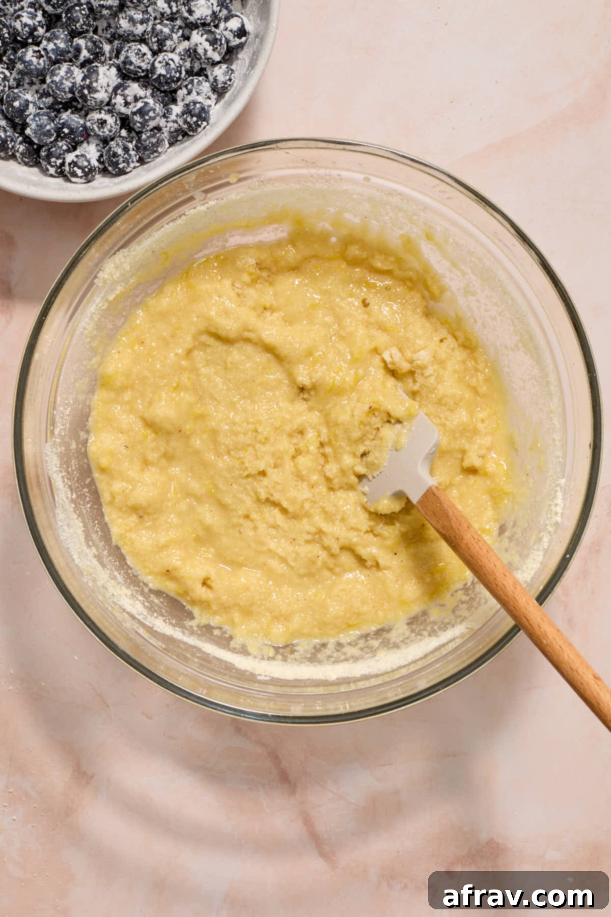 Bread batter mixed together in a glass bowl with blueberries coated in cornstarch on the side.