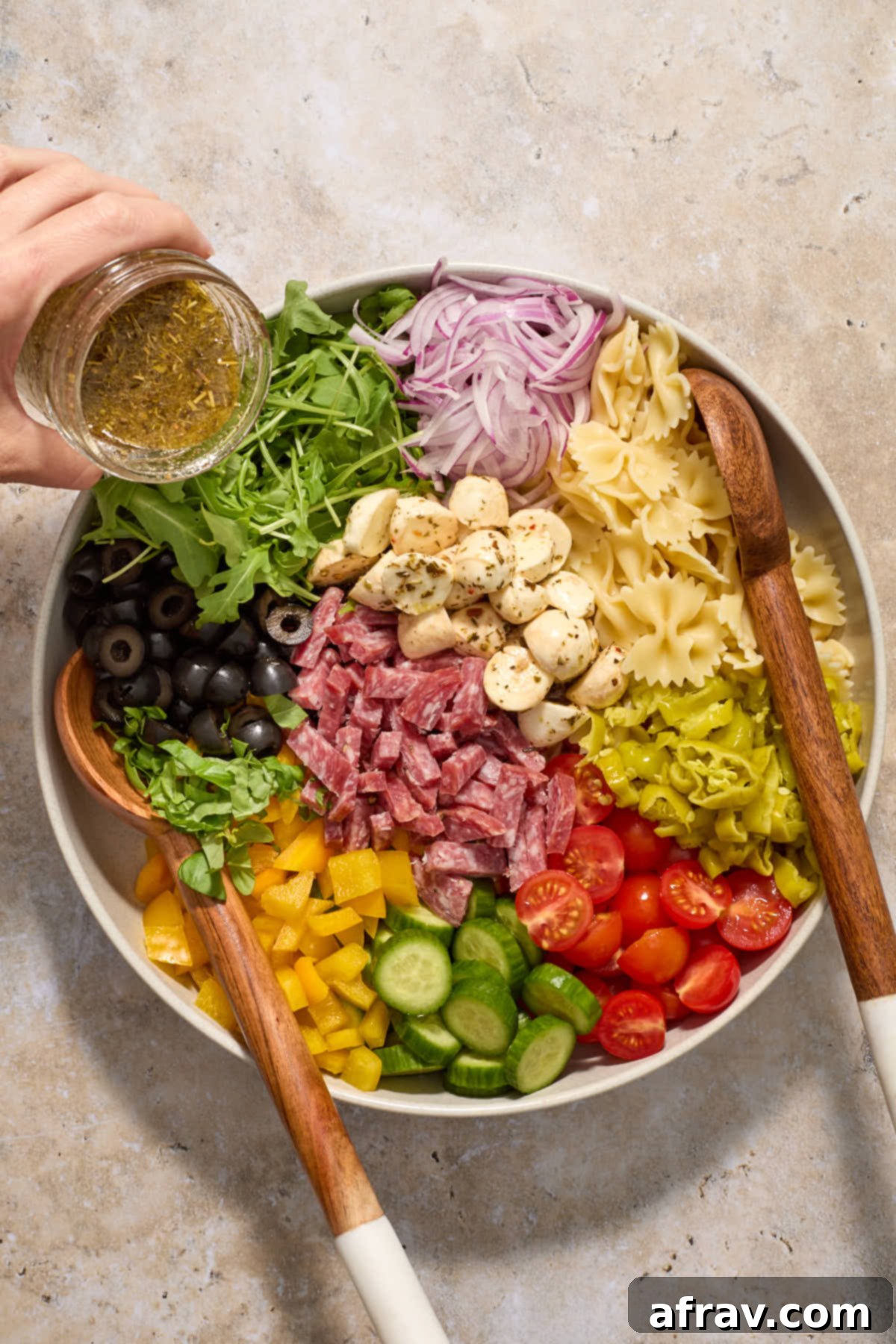 A large mixing bowl filled with various chopped salad ingredients, with homemade vinaigrette being poured over them.
