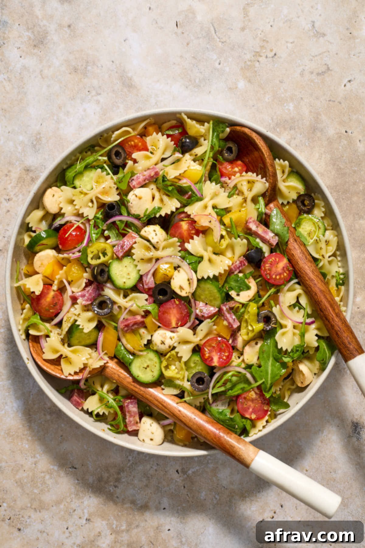 Italian pasta salad being tossed with wooden salad servers to evenly coat with dressing.