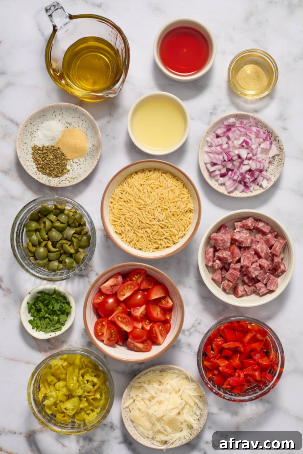 Various ingredients for Italian Orzo Salad and its dressing, including orzo, tomatoes, olives, salami, and dressing components, prepped in small dishes.