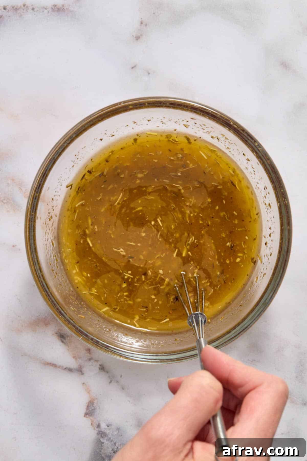 Homemade Italian dressing being whisked in a small glass bowl, showing the emulsification process.