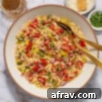 A top-down view of a bowl of Italian orzo salad with fresh ingredients, ready to be served, accompanied by dressing, parmesan, and herbs.