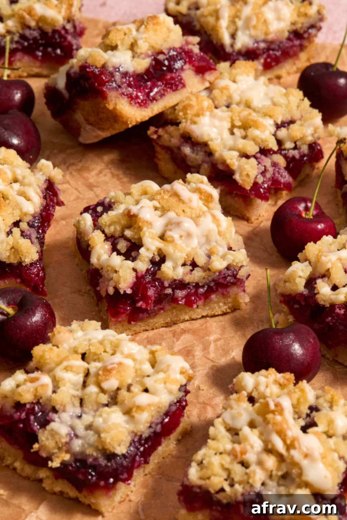 Cherry pie bars beautifully arranged on parchment with fresh cherries scattered around them.