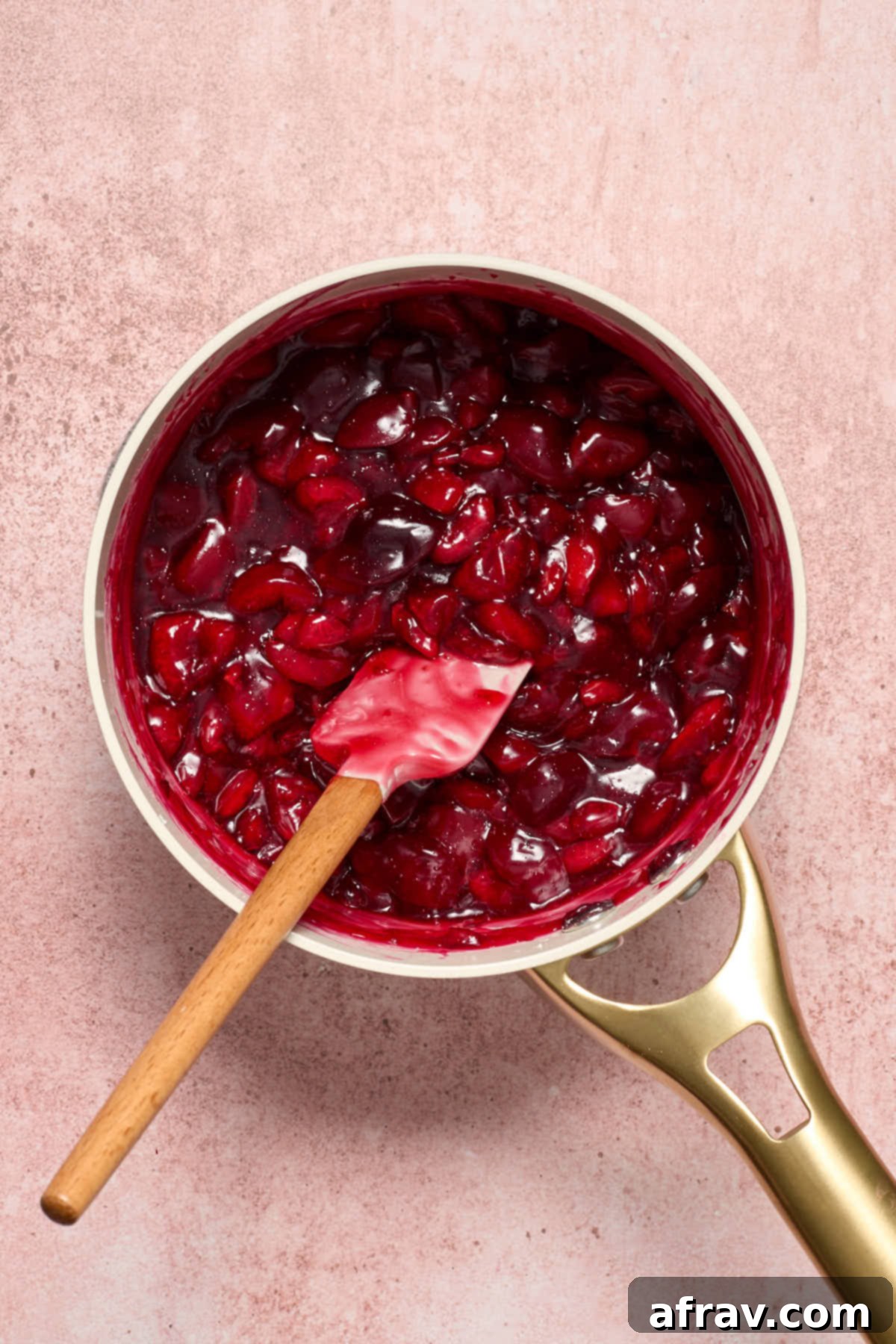 Cooked cherry pie filling in the saucepan, visibly thickened, with a spatula.