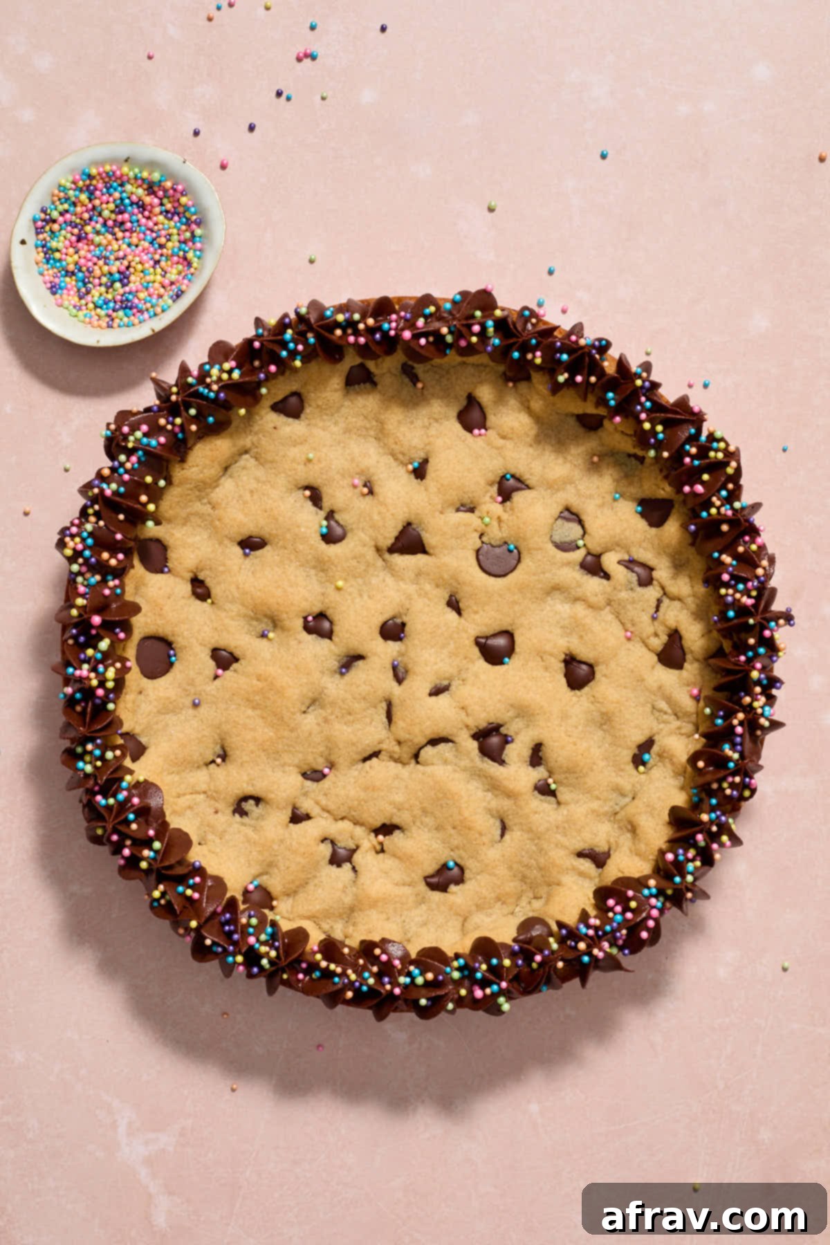 Frosting piped around the edges of the cookie cake with sprinkles on the side.
