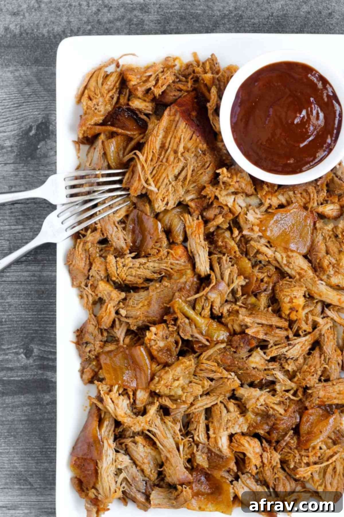Pulled pork with a side of BBQ sauce on a serving tray.