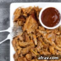 Pulled pork with two forks and a side of BBQ sauce on a plate.