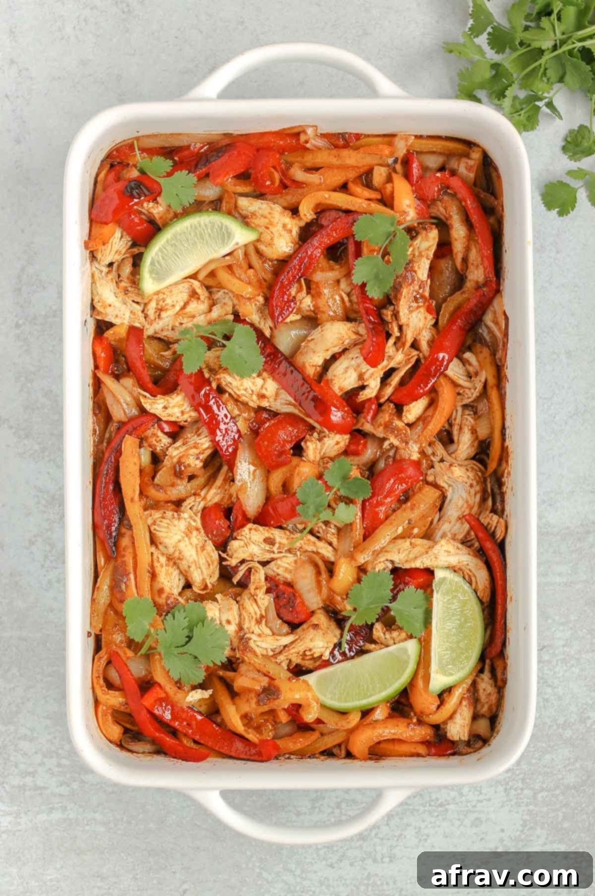 Sheet Pan Fajitas 6 Cooked shredded chicken mixed with tender-crisp peppers and onions, all combined in a white baking dish, ready to serve.