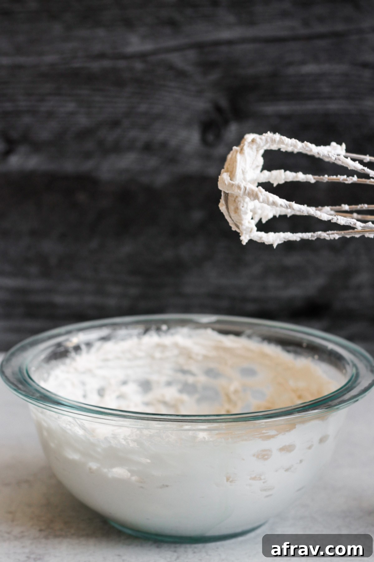 Electric beater with perfectly whipped coconut cream standing over a mixing bowl, showcasing its fluffy texture.