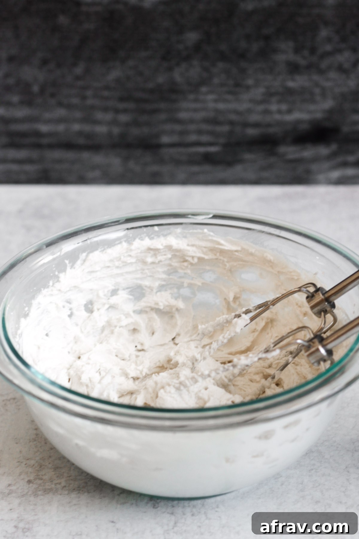 Side angle view of coconut whipped cream in a glass mixing bowl with electric mixer whisks, demonstrating its whipped texture.