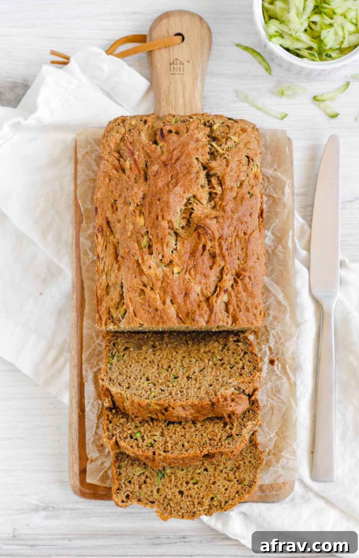 A beautifully baked loaf of gluten-free zucchini bread, half-sliced on a wooden cutting board, revealing its soft and moist texture.