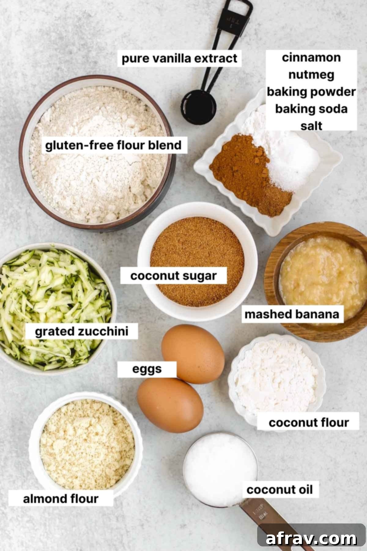All the labeled ingredients laid out for making gluten-free zucchini bread, including flours, spices, eggs, banana, and zucchini.