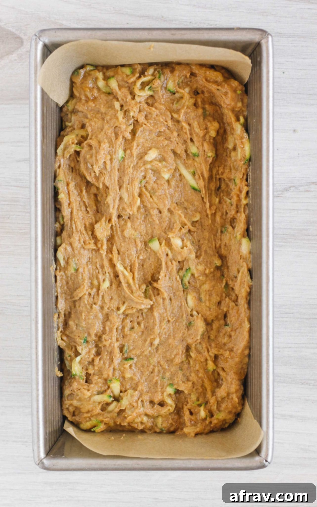 Raw zucchini bread batter in a loaf pan, smoothed on top, ready for baking.