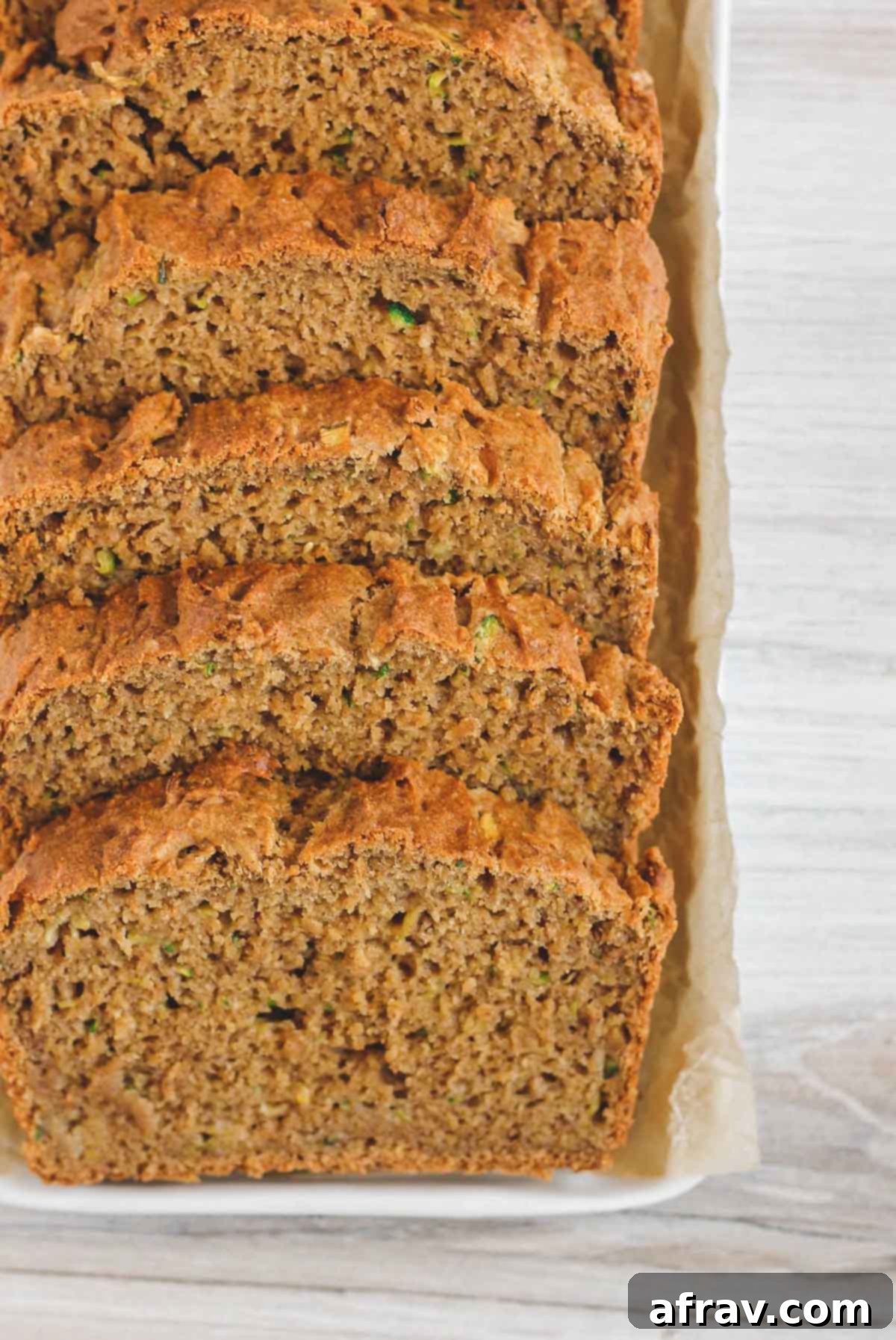 A slice of gluten-free zucchini bread on a cutting board, revealing its soft, moist, and fluffy interior texture with specks of zucchini.