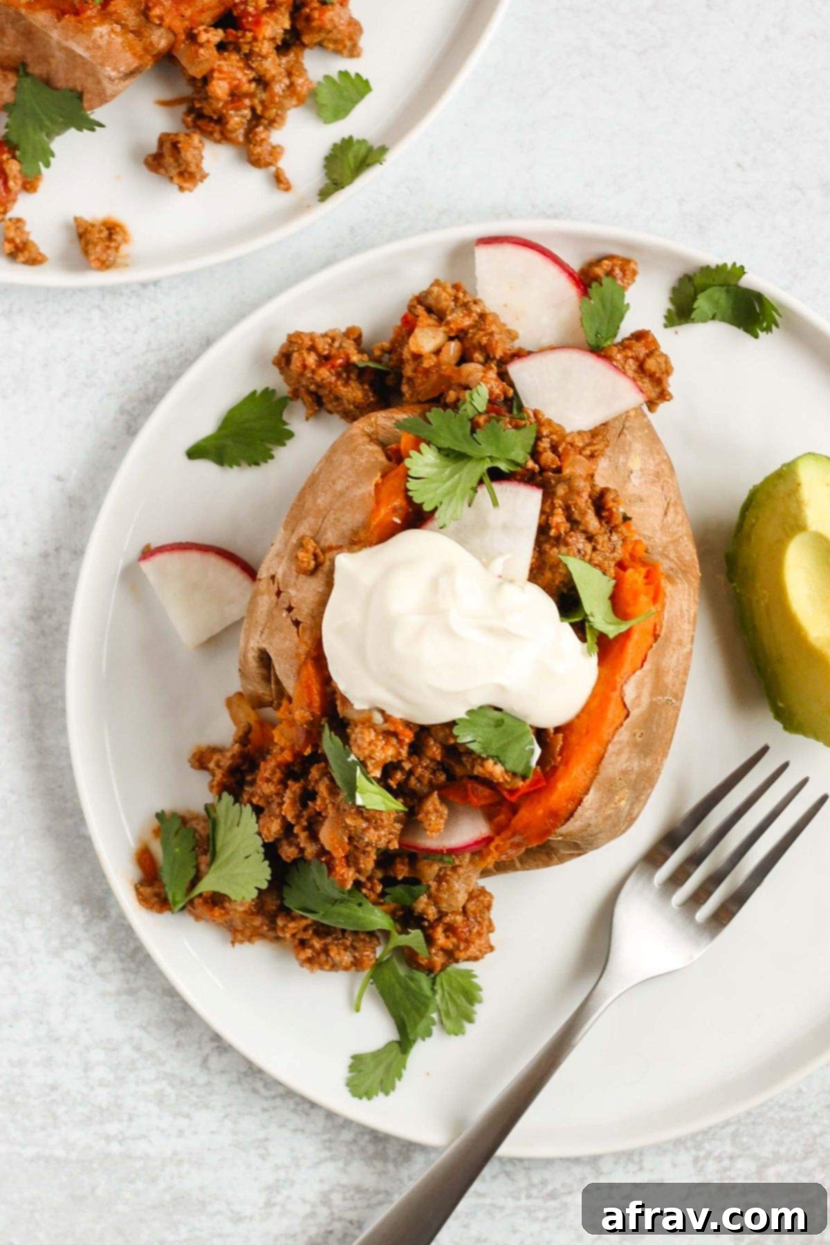 Chili stuffed sweet potato topped with sour cream, cilantro, and radishes with avocado on the side.