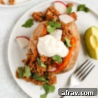 Chili stuffed sweet potato topped with sour cream, cilantro, and radishes with avocado on the side.