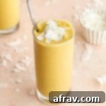 Mango smoothies in tall glasses and arranged on a pink surface with coconut chips scattered around.