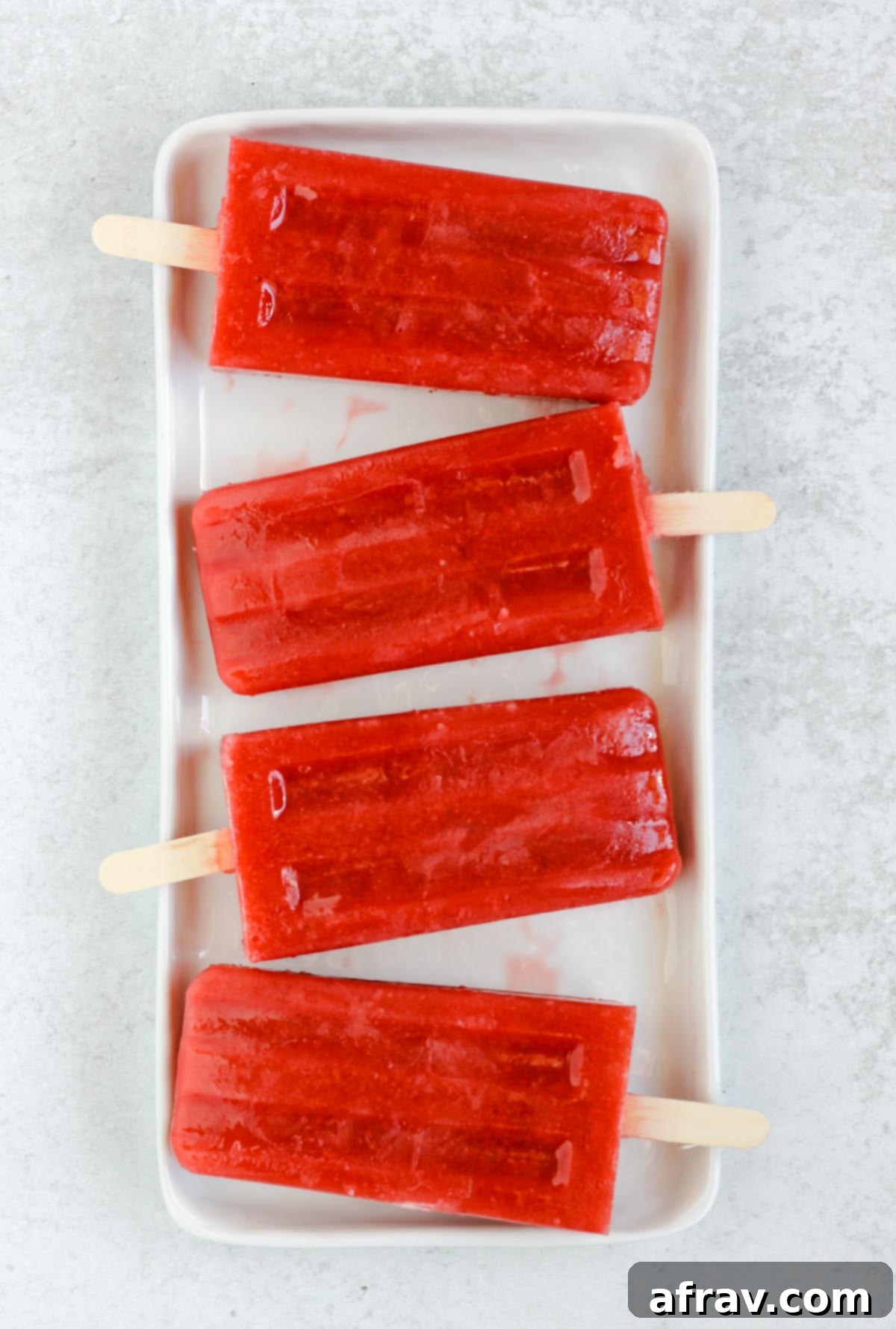 Simple 2-Ingredient Strawberry Watermelon Popsicles 4 white rectangle plate with four strawberry popsicles laid on plate